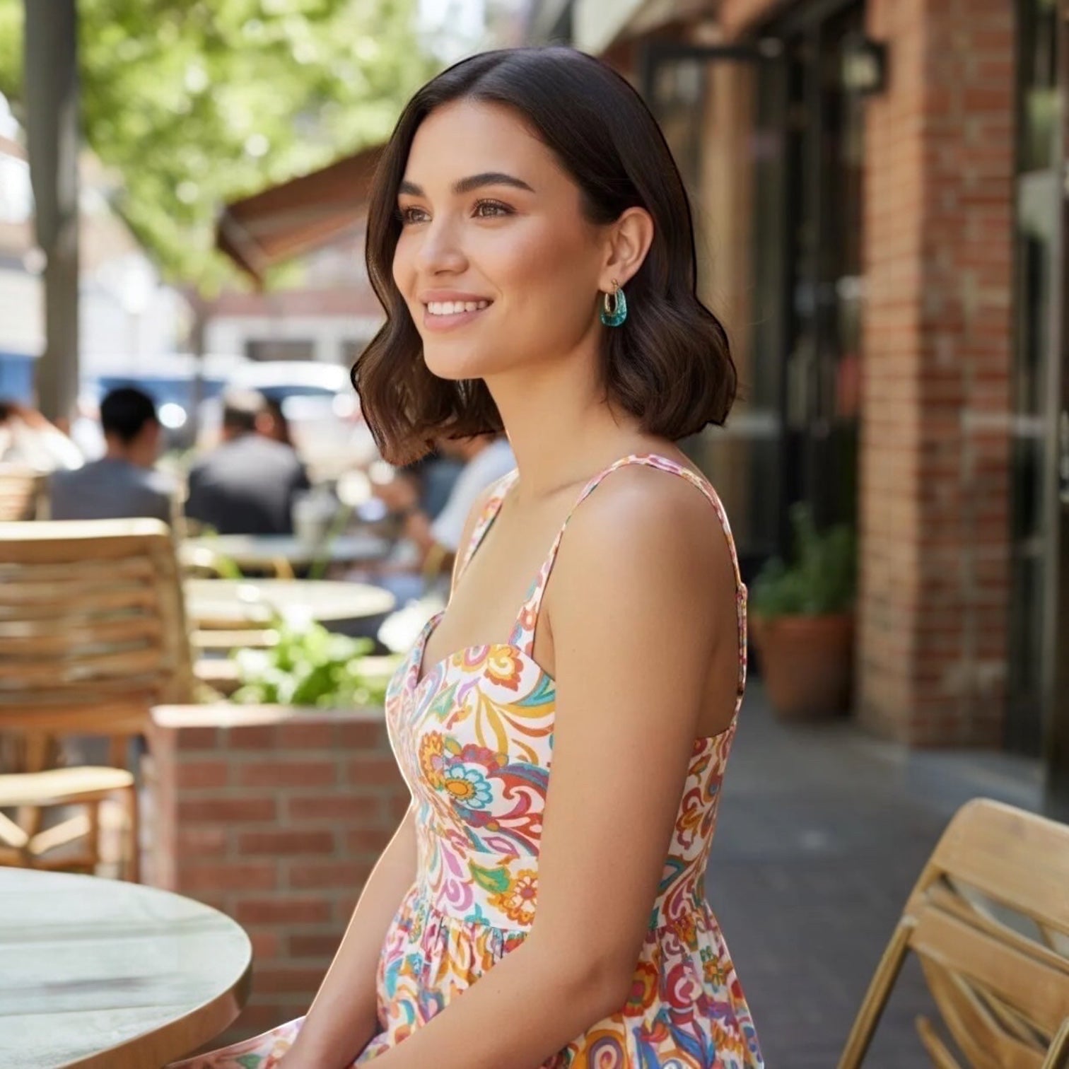 Chévereh gold-tone and teal resin sculptural hoop earrings worn by a woman outdoors.