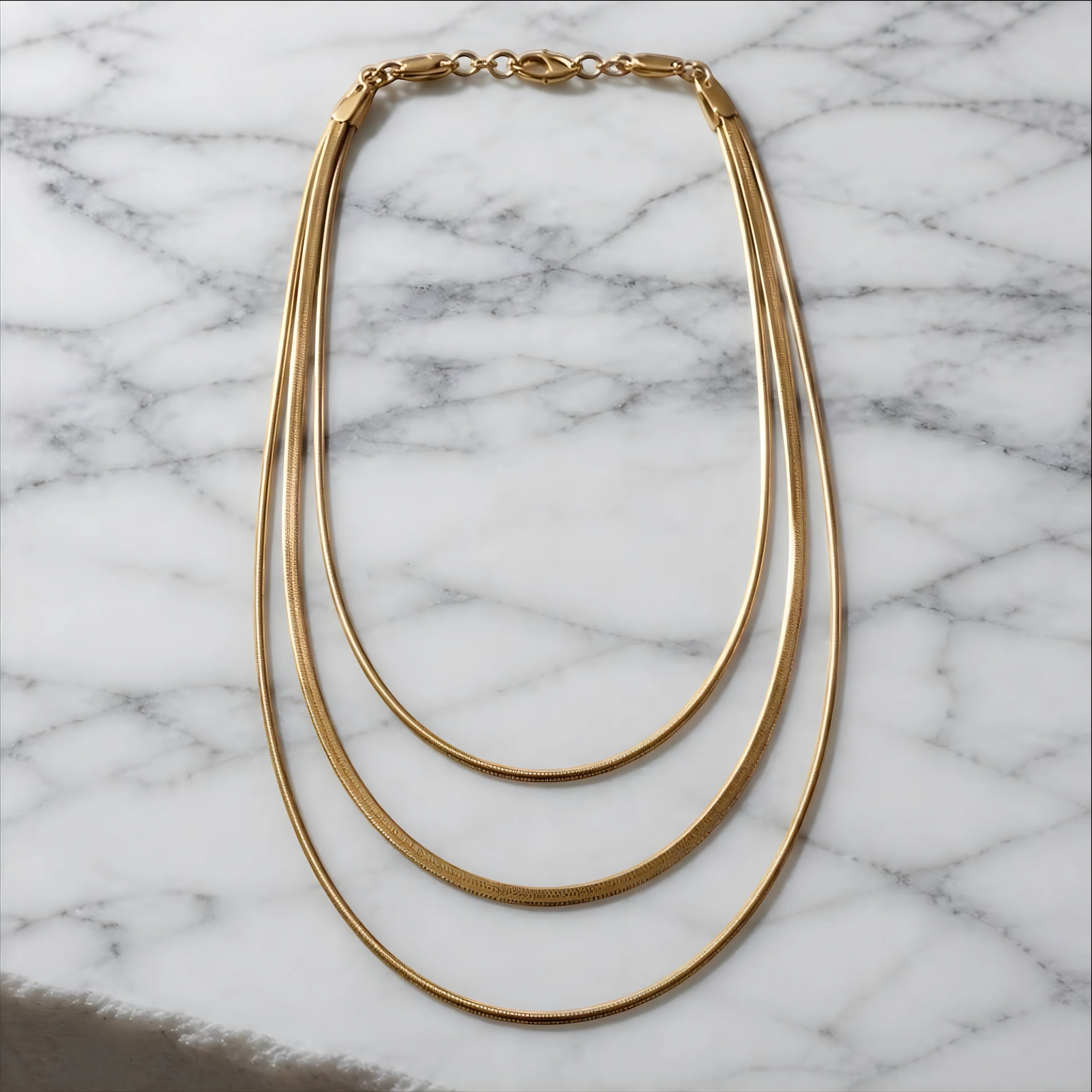 Chévereh gold-tone layered necklace featuring three delicate snake chains on a white marble surface.
