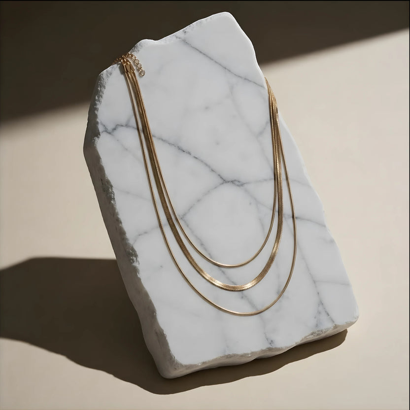 Chévereh three-layer gold-tone chain necklace displayed on a white marble slab for a modern, elegant look.