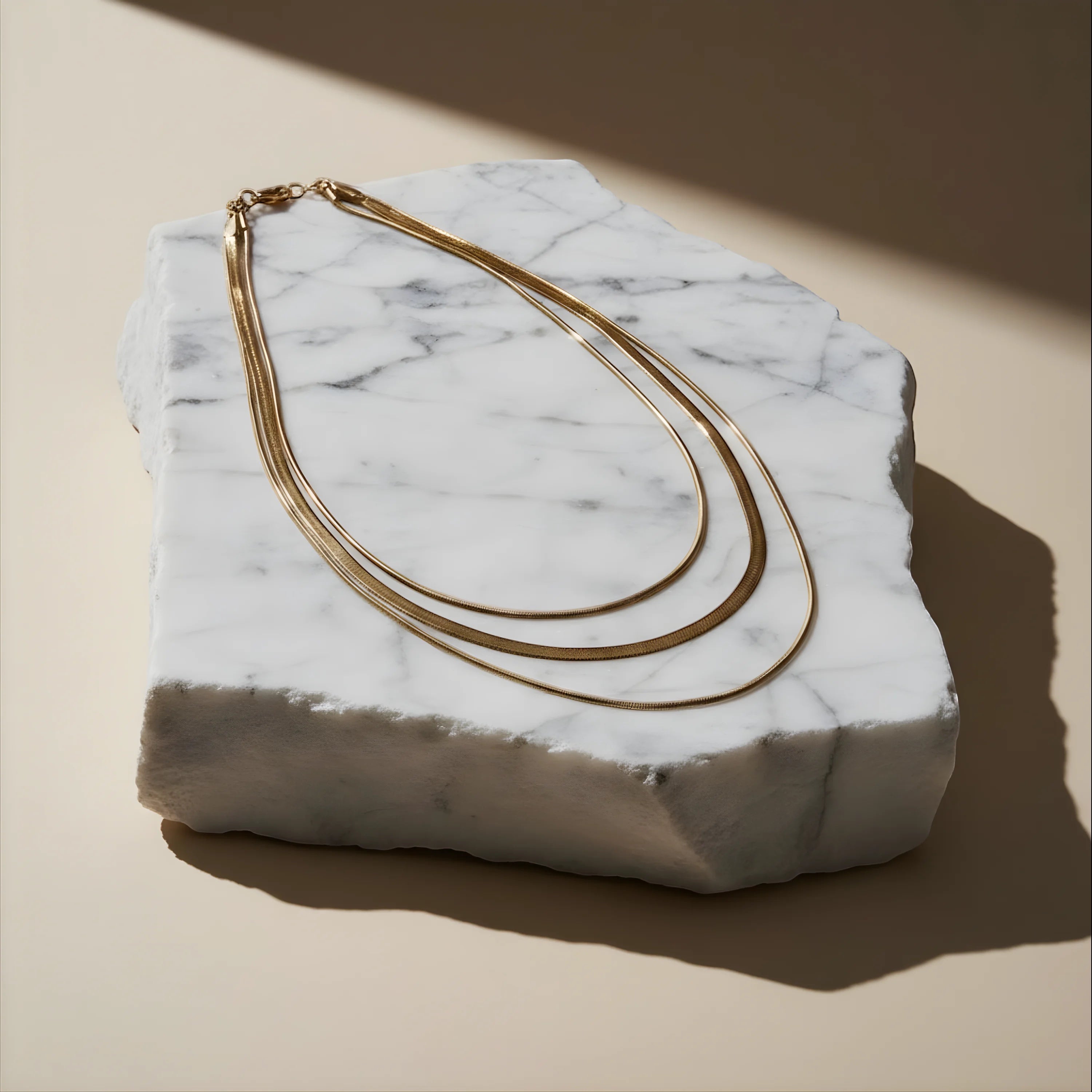 Chévereh three-layer gold-tone chain necklace with a sleek, modern design displayed on a white marble stone block.