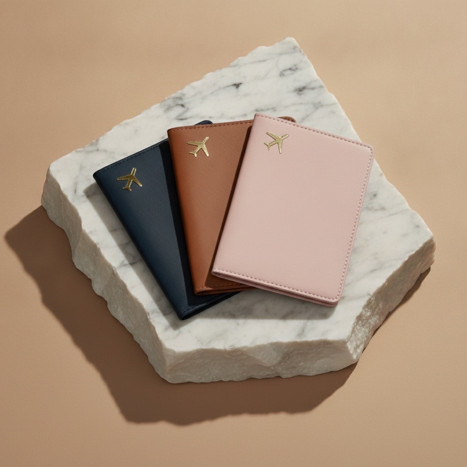Chévereh PU leather passport holders in black, brown, and pink with gold airplane emblems on a marble display base.