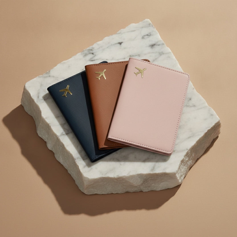 Chévereh PU leather passport holders in black, brown, and pink with gold airplane emblems on a marble display base.
