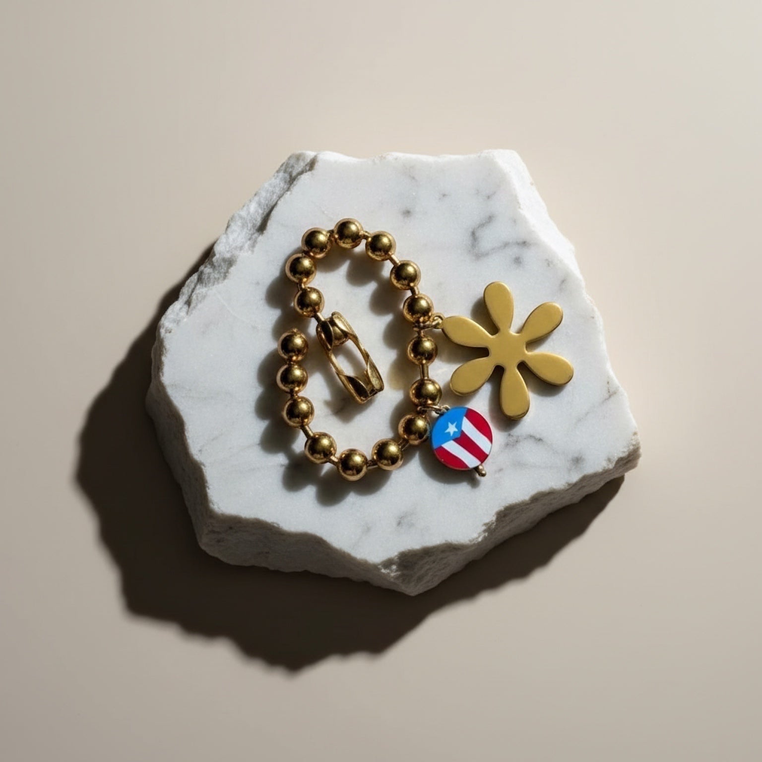 Chévereh gold-tone beaded bracelet with flower and Puerto Rico flag charms. Features spherical beads and a secure clasp.
